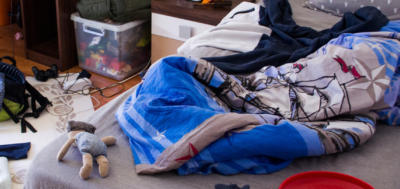 A messy room, focusing on the bed, with blankets all disogranized and junk laying around