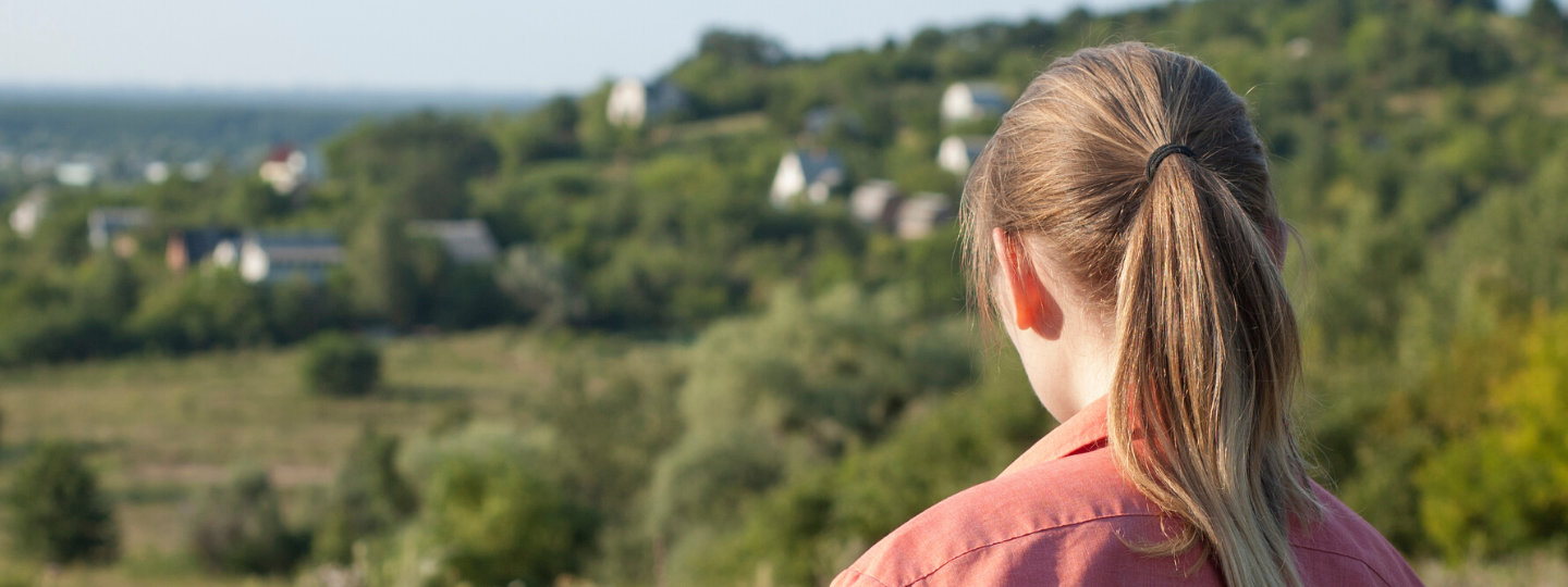 Back of a girl's head with her ponytail, looking out into a green terrain