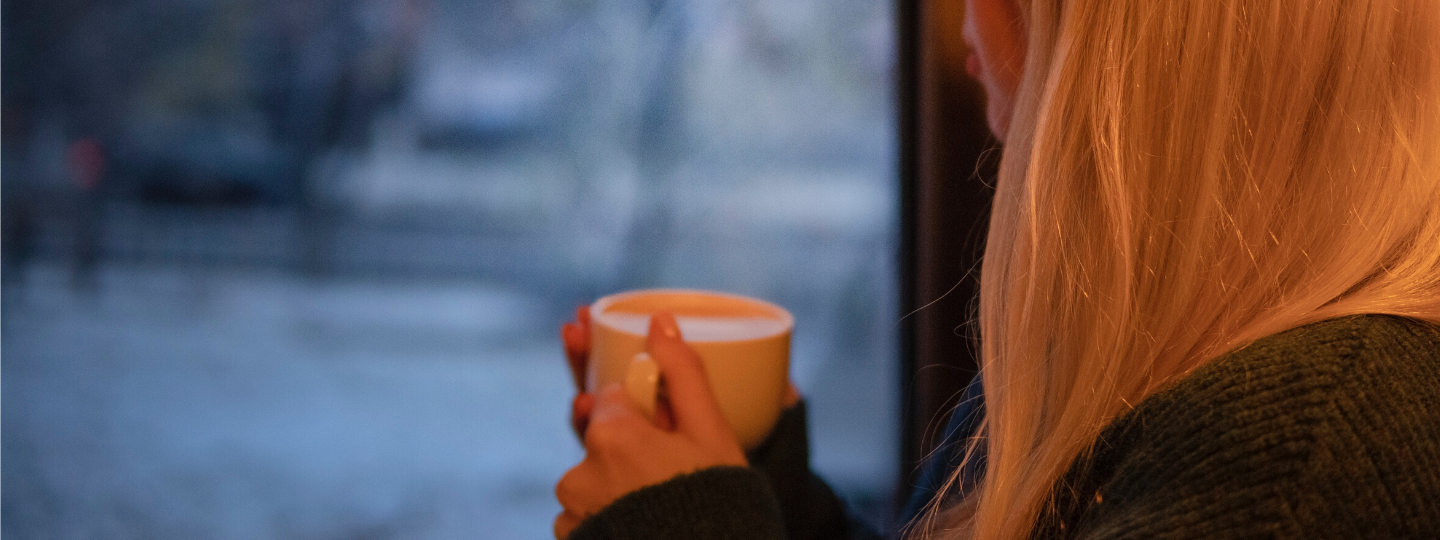 Close up of a woman holding a mug looking outside a window