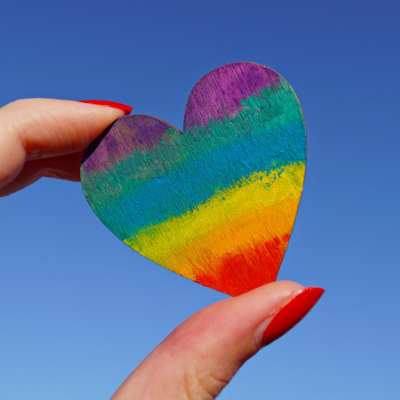 coming-out person holding a small rainbow heart