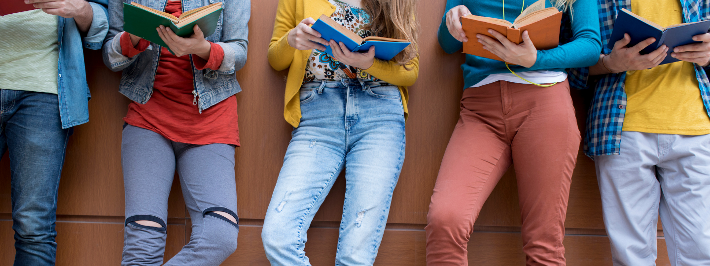 A group of students standing against a wall reading books
