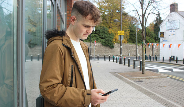 Young man looking at his phone standing on the pavement of the street