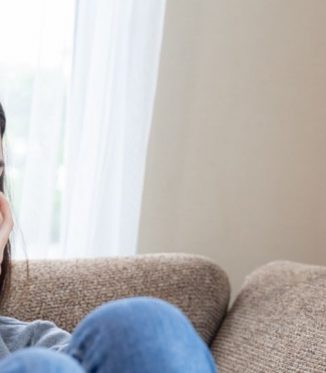 Dark haired girl sitting on couch looking out into the distance looking sad