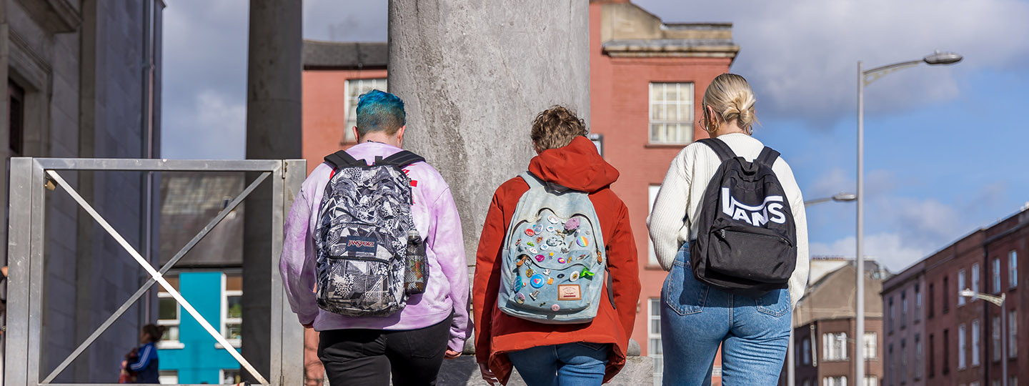 Three young people walking up steps with rucksacks on their backs - shot taken from behind