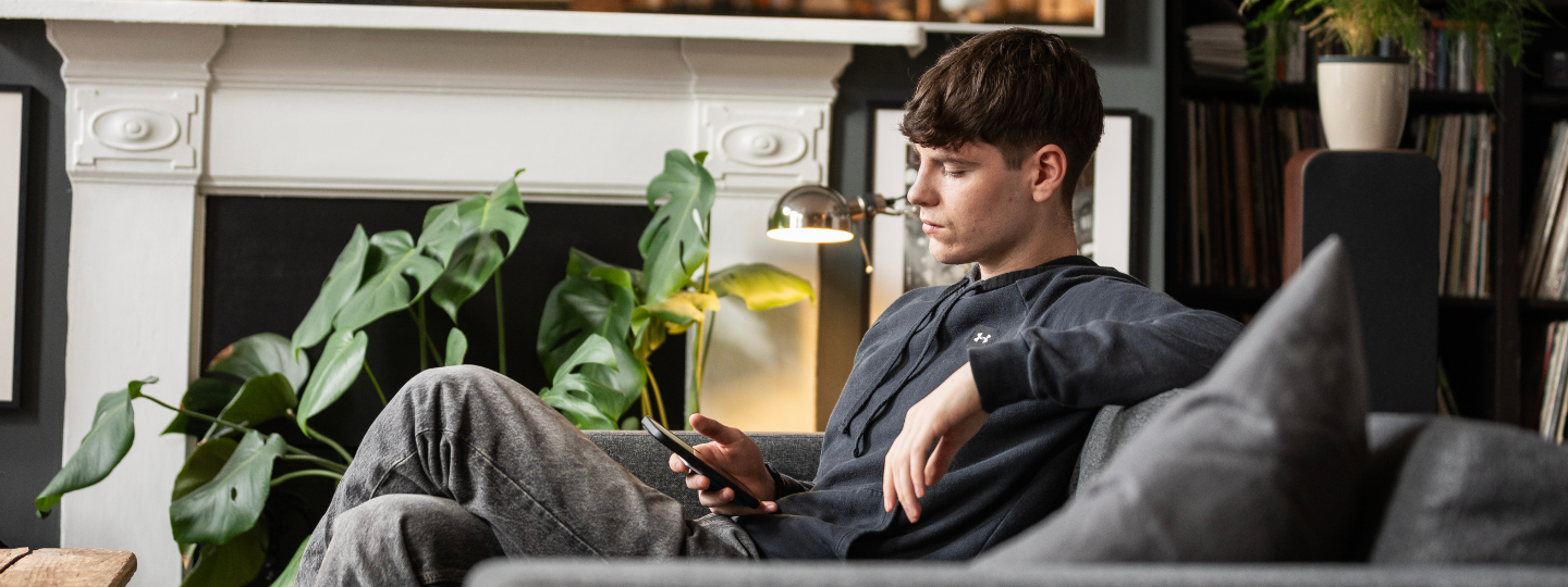 young adult looks at phone sitting on couch